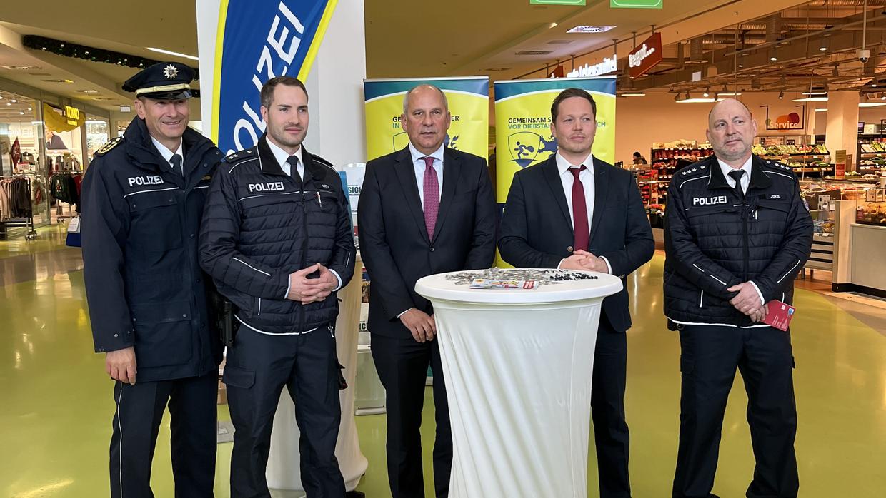 Innenminister Roman Poseck zusammen mit Polizeipräsident Michael Tegethoff und Projektleiter "Sicherheit im Handel" Benjamin Becker mit den Schutzleuten vor Ort am Informationsstand im Einkaufscenter Emaillierwerk anl. Aktionstag Diebstahlsprävention.